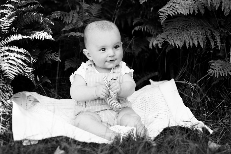 baby sitting in front of some ferns.