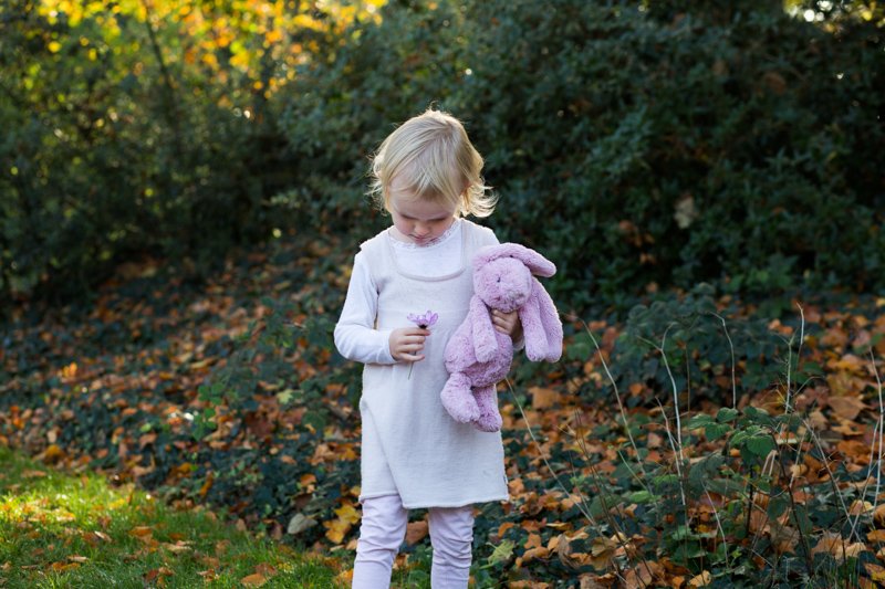 Little girl with pink toy rabbit looking down at flower. 