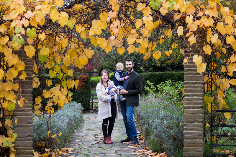Family of four smiling in arch of Autumn leaves. 