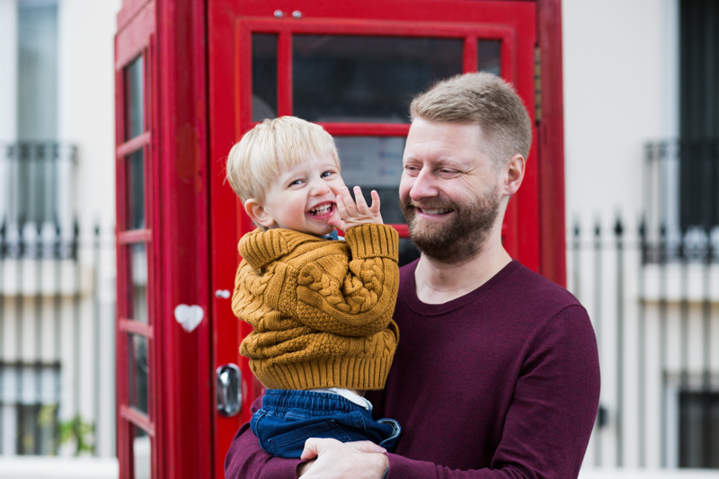 Dad and son laughing in front of red phone box. 