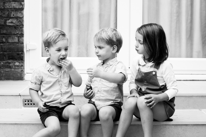 One boy eating something while two children watch him. 