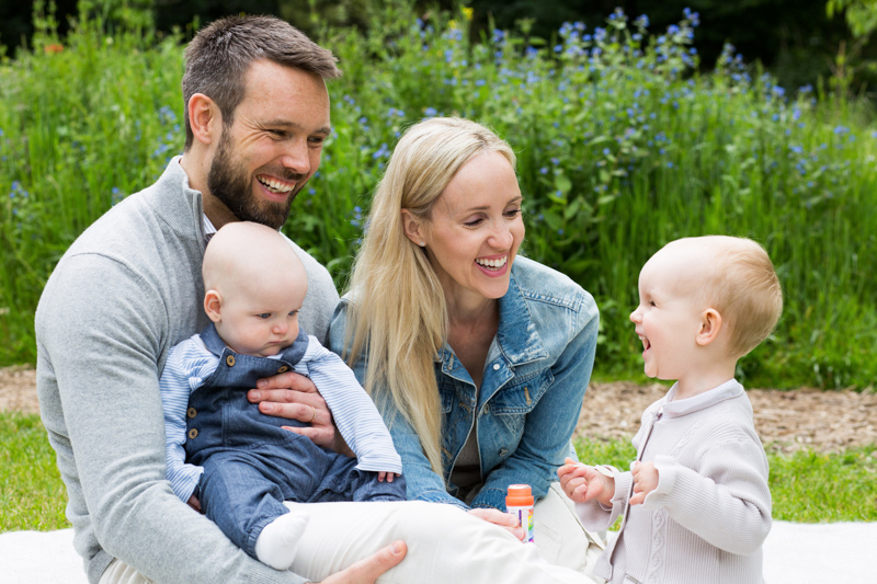 Mum, dad, little girl and baby smiling in front of blue flowers and grass