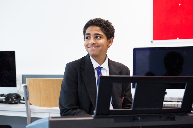 Boy sitting at a keyboard smiling. 