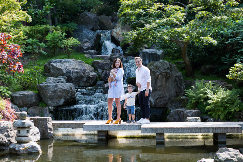 Mum, dad, boy and baby standing by some water with a waterfall behind them. 