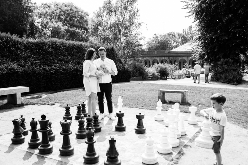 Mum and Dad holding their baby by huge chess set. 