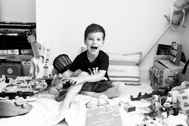 Little boy sitting amongst his toys laughing. 