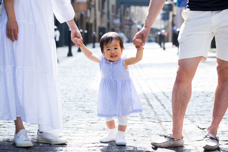 Little baby girl holding hands with her parents in a cobbled street. 