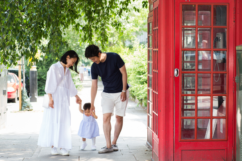 Little girl walking with her parents next to red London telephone box. 