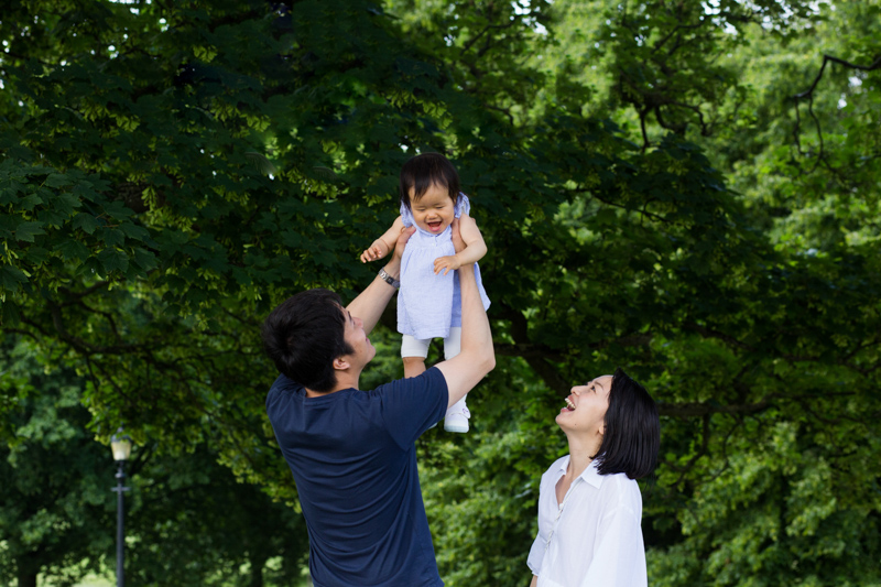 Dad lifting his baby girl in the air with mum looking on. 