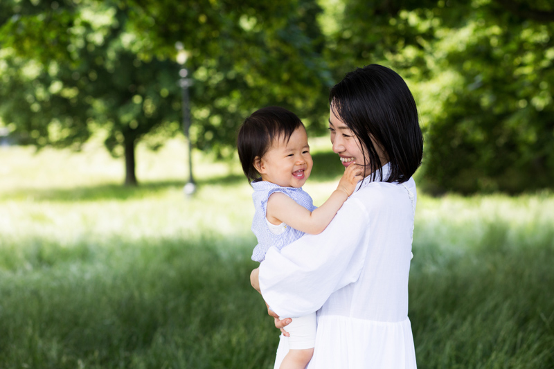 Lady and baby smiling in front of trees. 