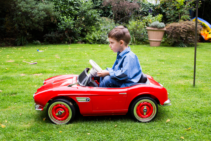 Little boy in blue shirt driving toy red car. 