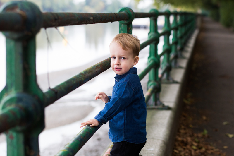 Boy standing by the river holding onto green railings. 