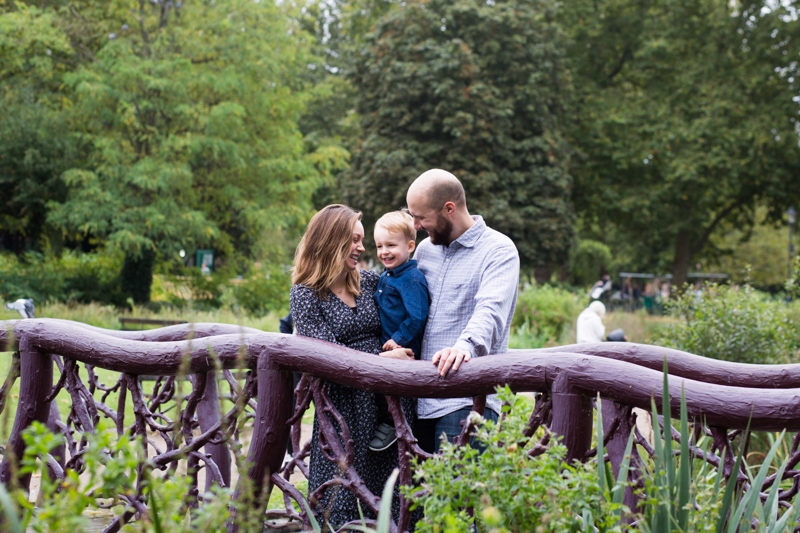 Family of three on wooden bridge with trees in the background. 