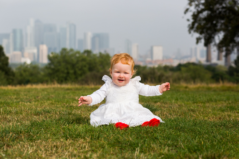 Baby girl with white dress and red socks in front of city view. 