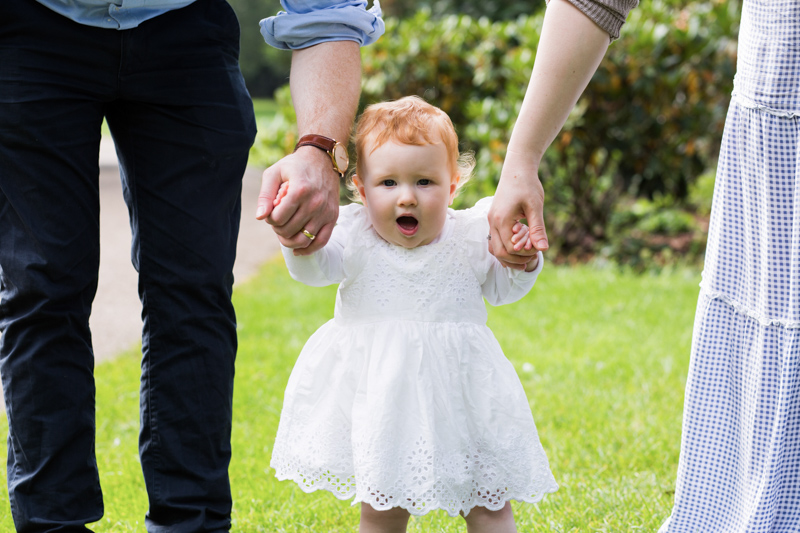 Baby in white dress holding hands with grown ups