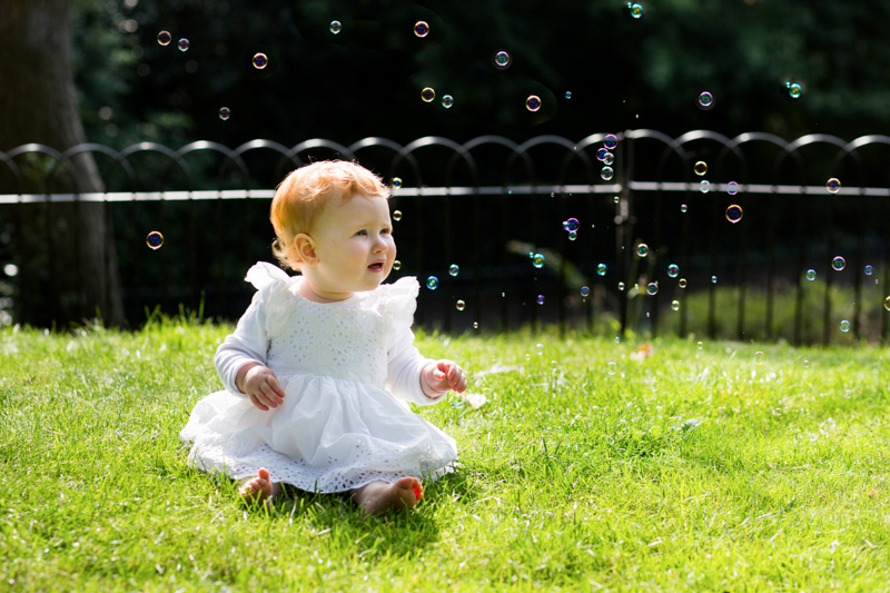 baby sitting on grass looking at bubbles
