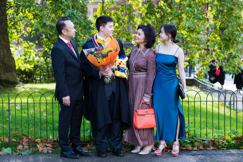Family of four standing together, one man in graduation gown. 