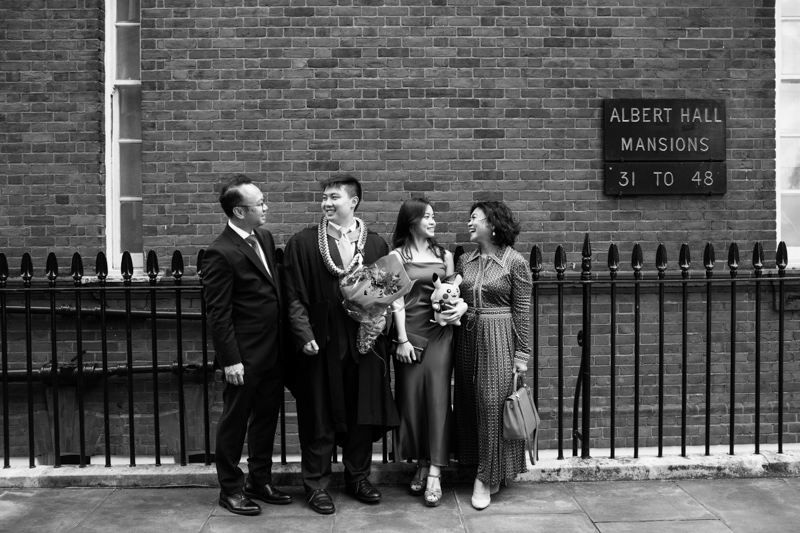 Family of four looking at each other in front of brick wall. 