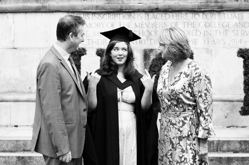 Three people talking, the one in the middle wearing graduating gown and mortar board. 