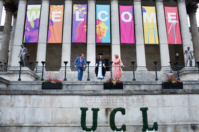 Three people standing under WELCOME banner and above UCL sign. 