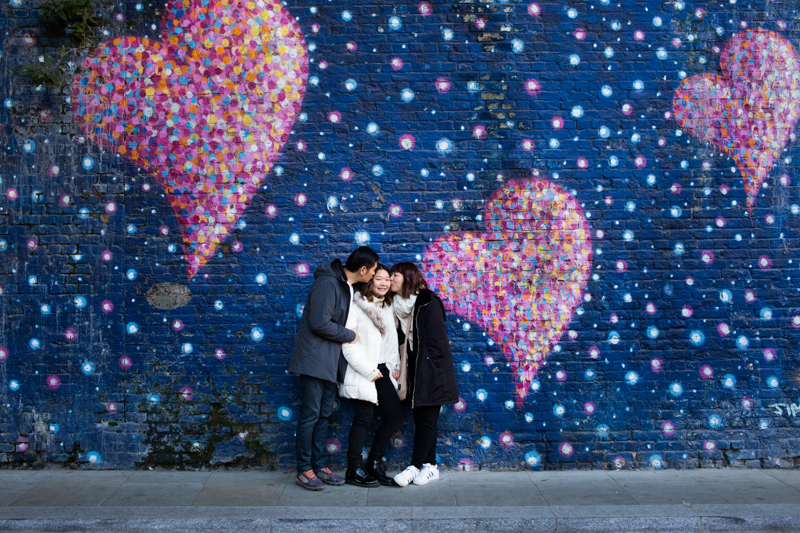 Family of three in front of wall of painted hearts. 
