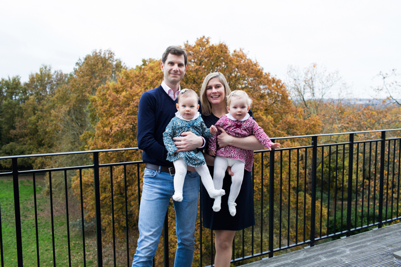 Family of four on balcony in front of Autumn trees. 