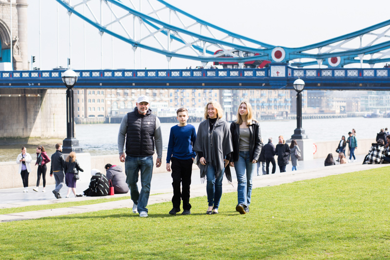 Four people walking across grass with Tower Bridge behind them. 