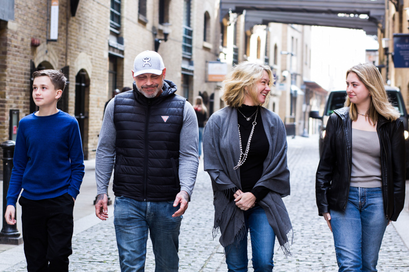 Family of four walking along a cobbled street with warehouses either side. 