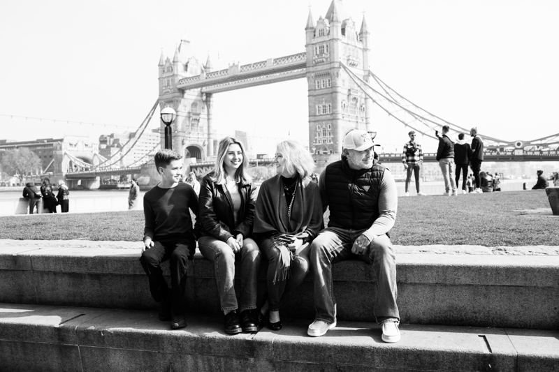 Man, lady, boy and girl sitting down with Tower Bridge in the background. 
