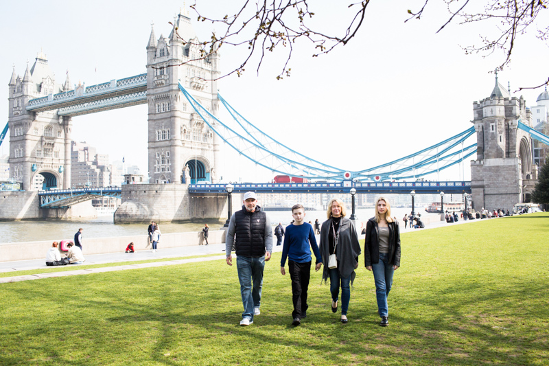 Family of four walking across the grass with Tower Bridge in the background. 