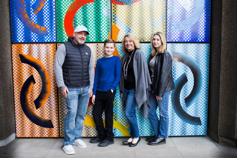 Family of four smiling in front of colourful wall. 