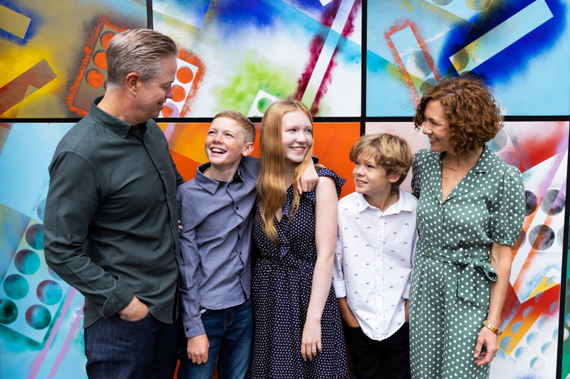 Family of five smiling at each other in front of a colourful wall