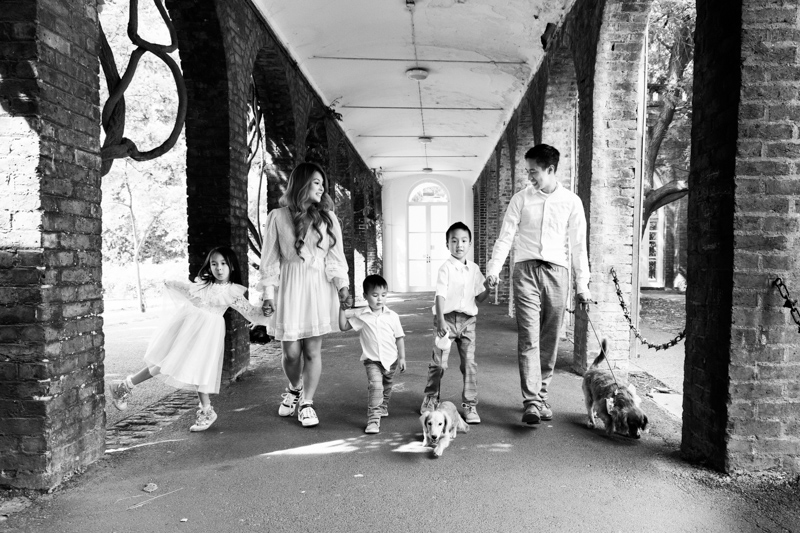 Family of five and two dogs walking on a path with arches either side of them. 