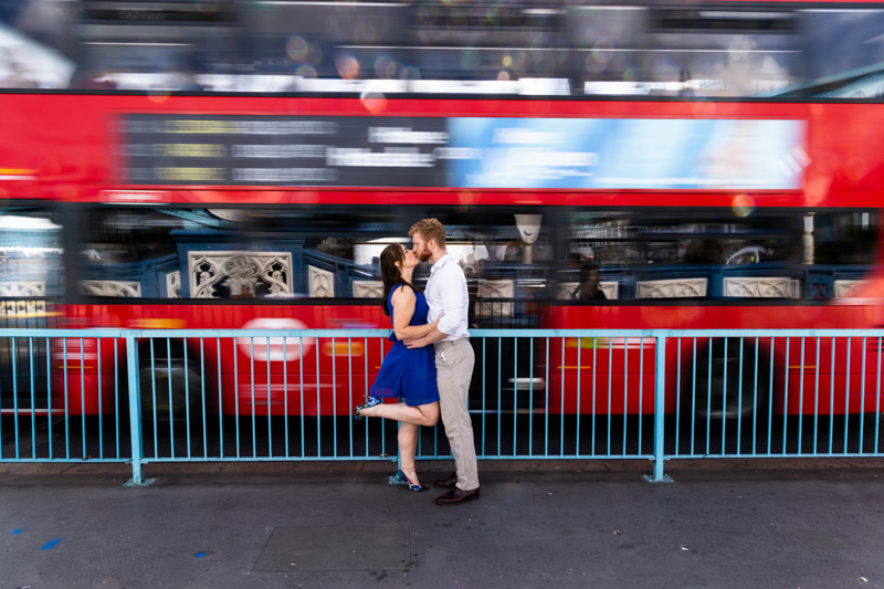 Lady (with one raised leg) kissing a man in front of a blurred bus. 