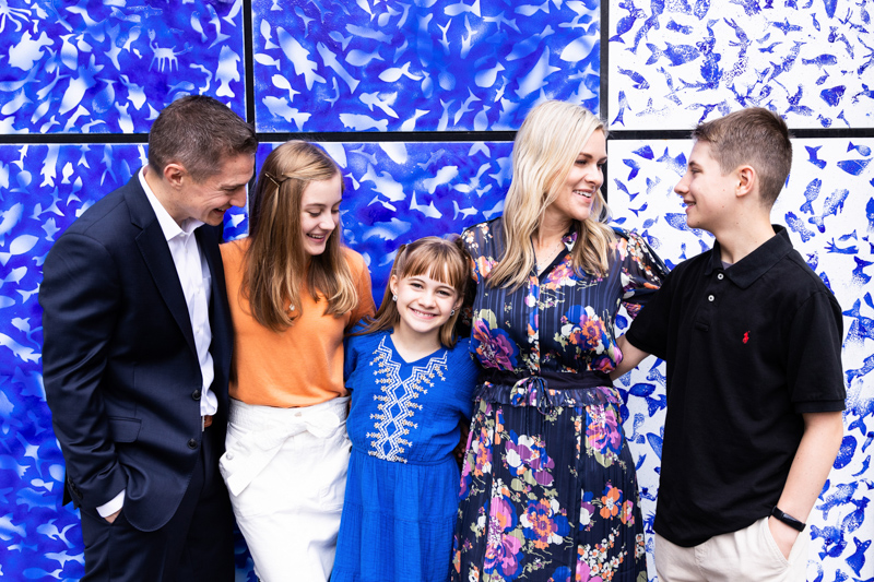 Family of five standing in front of blue and white patterned wall. 
