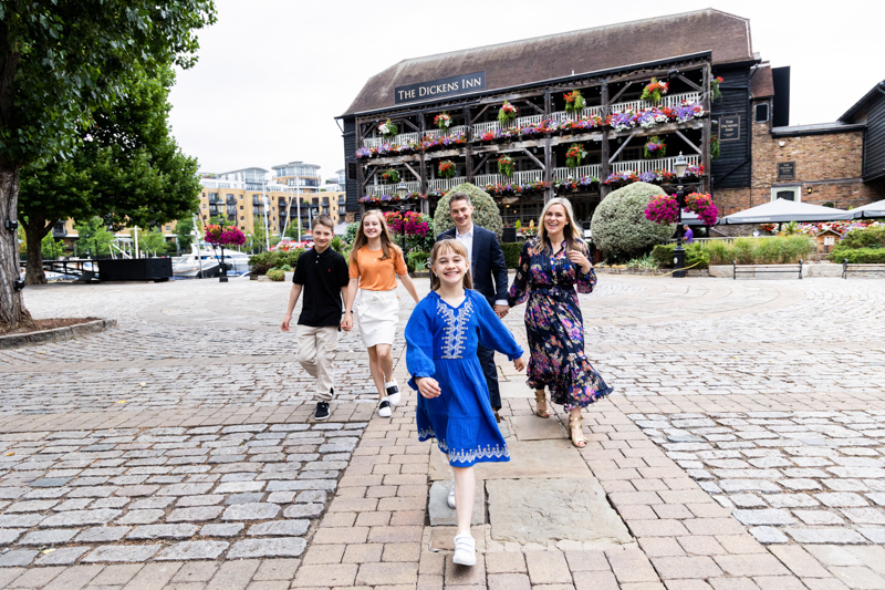 Girl in blue dress leading her family, with The Dickens Inn in the background. 