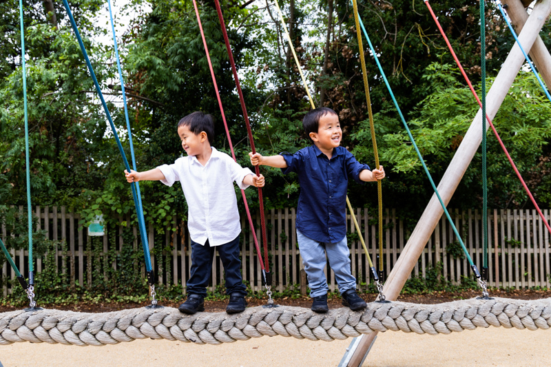 Twin boys playing on a colourful swing in a playground. 