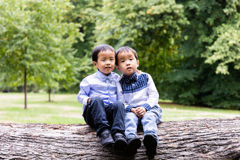 two twin boys sitting on large tree trunk