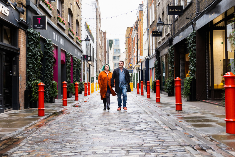Couple walking down a cobbled street with colourful bollards 