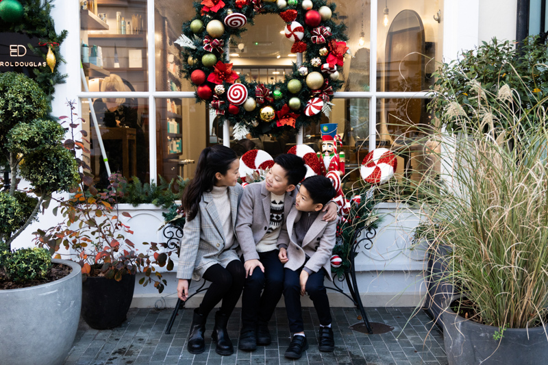 Three children sitting under a large Christmas wreath