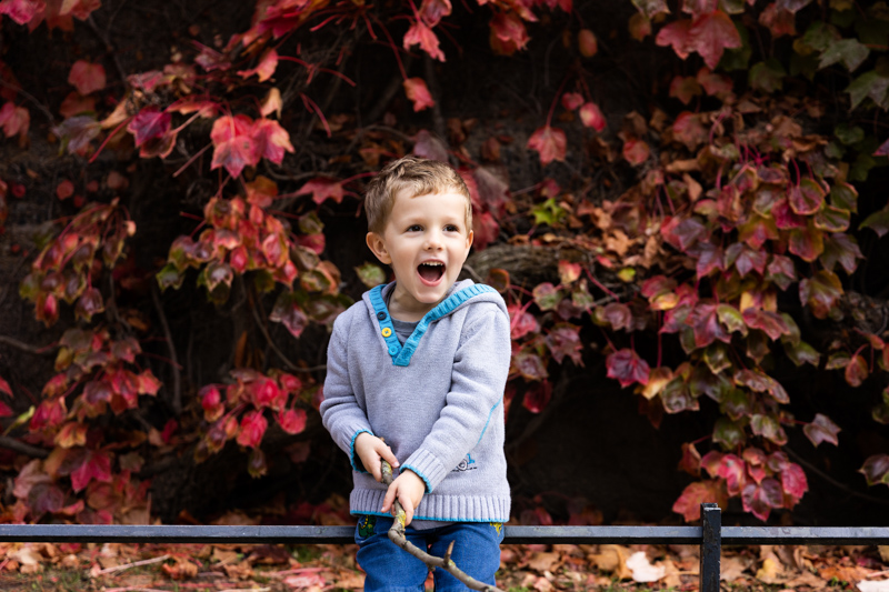 Boy laughing in front of red autumn leaves
