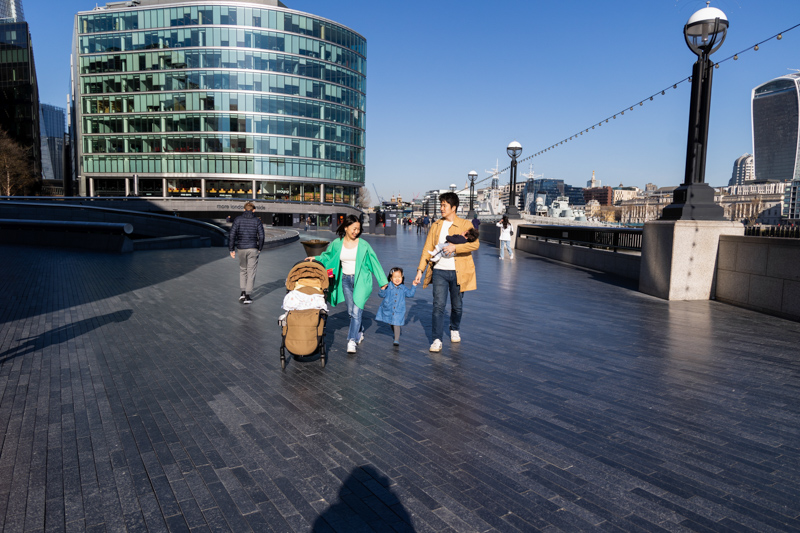 Mum, dad, girl and baby walking in front of City Hall by the River Thames.