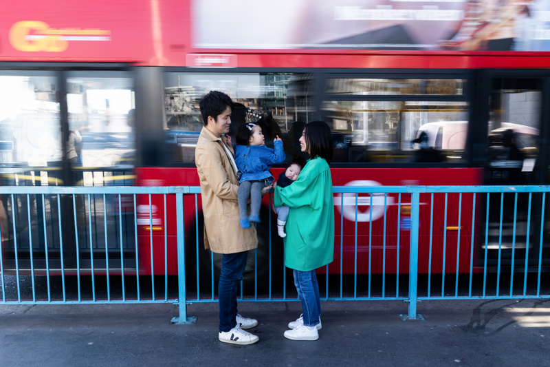man, lady, girl and baby standing in front of moving bus