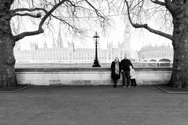 Mum, dad and young son surrounded by trees, with Houses of Parliament behind them. 