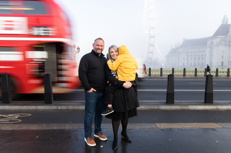 family of three with red bus and the London Eye in the background