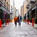 Couple walking down a cobbled street with colourful bollards