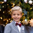 Smiling boy wearing a bow tie, in front of a Christmas tree