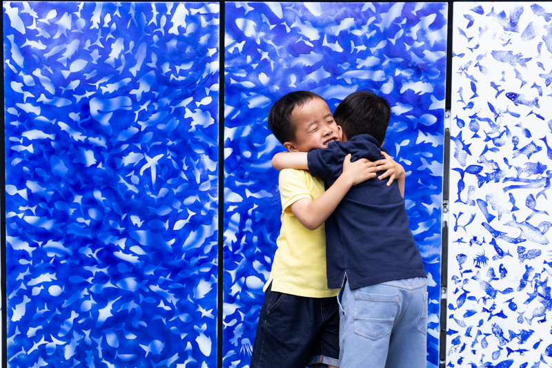 two boys hugging in front a blue patterned wall