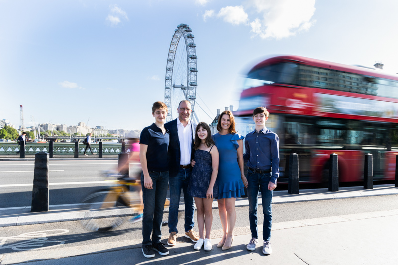 a man, lady, two boys and a girl with a red bus behind them and the london eye