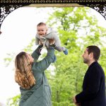 lady holding baby up in the air, while man looks on
